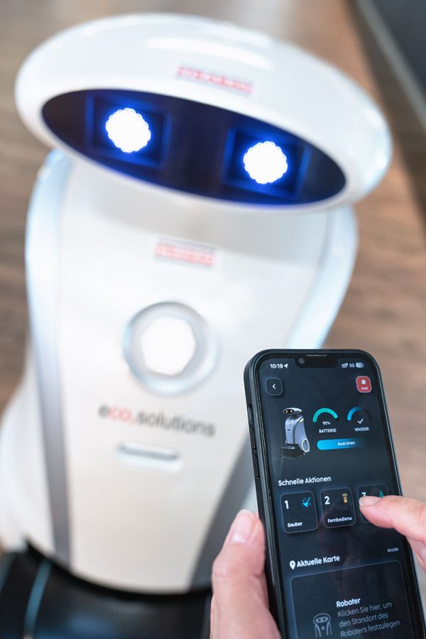 eco2solutions | Hand hält Handy mit eco2clean Reinigungsroboter App vor Roboter und überprüft den Weg